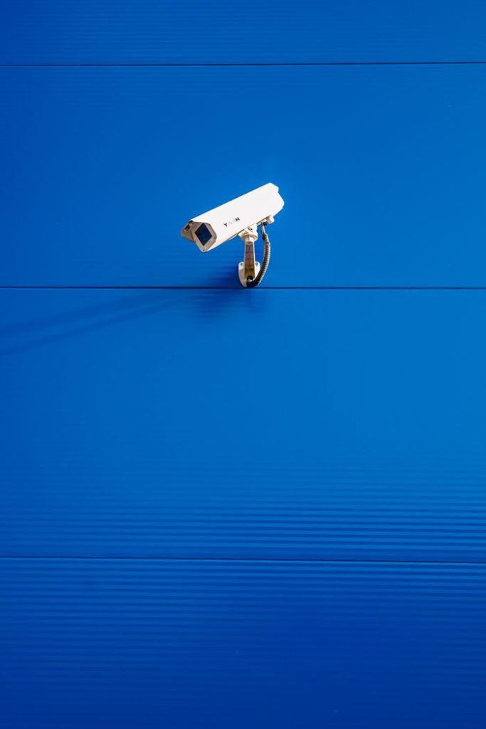 White security camera against a vibrant blue textured wall in a minimalist style.